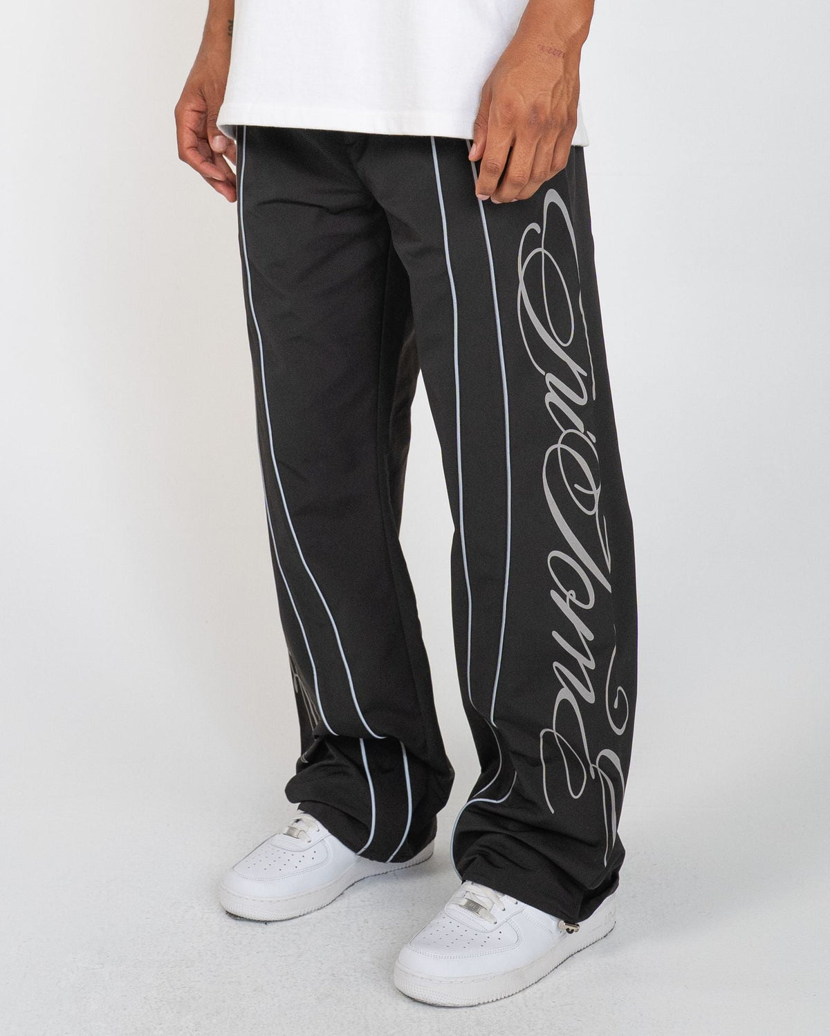 Black Monogram Men's Pants, black wide-leg with silver script monogram and piping, angled view on model