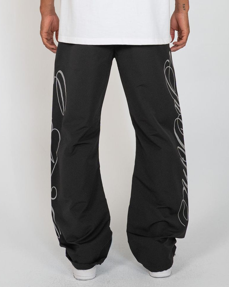 Black Monogram Men's Pants, black wide-leg with silver script monogram, back view on model